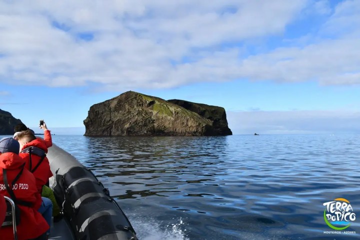 Boat approaching a large rock formation in the ocean under a cloudy sky.