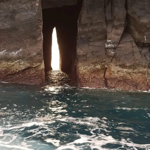 Narrow rock opening with ocean waves in the foreground.