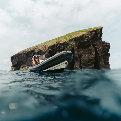 Boat near a rocky cliff with grassy top, partially submerged view.