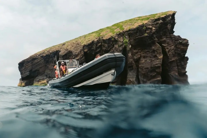 Boat near a rocky cliff with grassy top, partially submerged view.