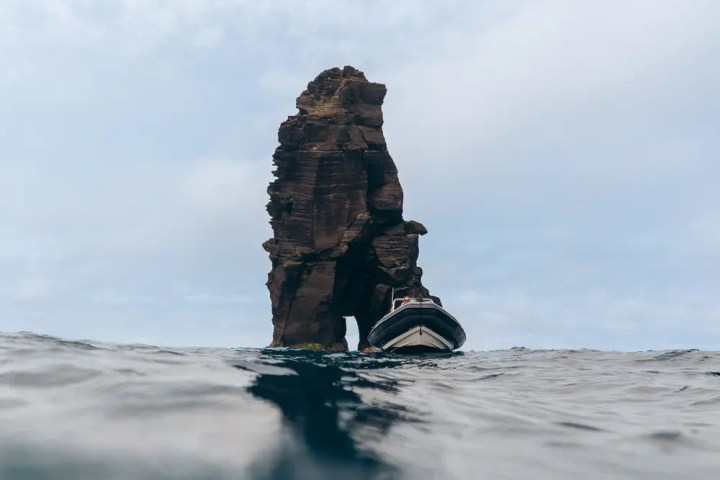Rock formation in ocean with small boat nearby under cloudy sky.