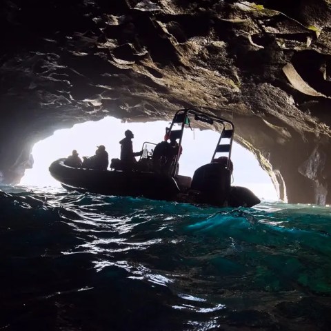Silhouette of a boat in a cave with sunlight at the entrance.