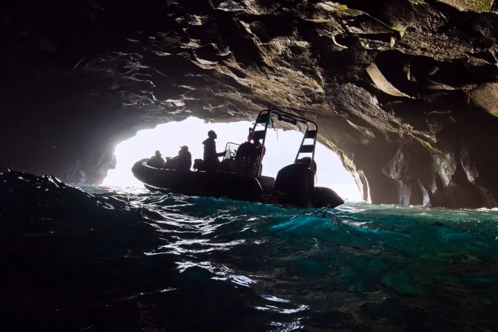 Silhouette of a boat in a cave with sunlight at the entrance.