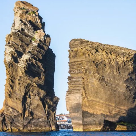 Two large rock formations rising from the sea under a clear blue sky.