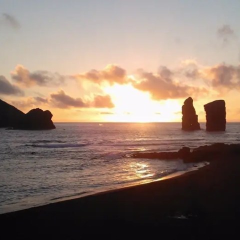 Sunset over the ocean with rock formations and clouds.