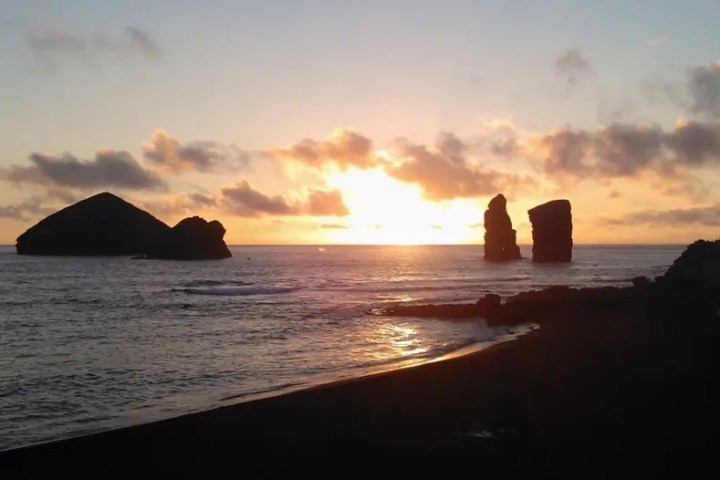 Sunset over the ocean with rock formations and clouds.