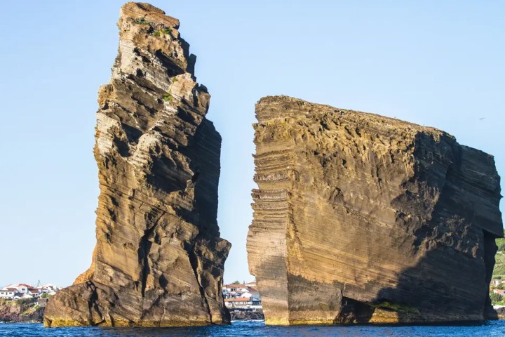 Two large, jagged rock formations rise from the ocean against a clear blue sky.