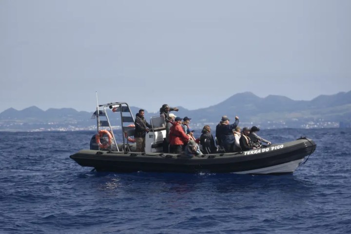 Group of people on a boat in the ocean with mountains in the background.